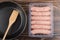 Raw chicken sausages in plastic container, spatula in frying pan