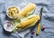 Raw corn cob and aromatic spicy butter on a blue background, top view.