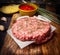 Raw cutlet for burger on cutting board with sauce, onions on wooden rustic background close up