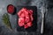Raw diced red beef meat for Goulash on marble board. Black background. Top view