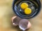 Raw double yolk organic chicken egg cracked open into small black bowl. Egg shell nearby.