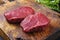 Raw dry aged bison beef rump steaks with herbs on a rustic wooden board