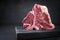 Raw dry aged wagyu porterhouse beef steak with large fillet piece on a black burnt wooden board