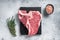 Raw dry aged wagyu porterhouse beef steak, uncooked T-bone on marble board with thyme. Gray background. Top view