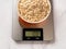 Raw dry oatmeal in a bowl on a digital kitchen scale. The scales displaying 100g of grits without tare. Modern electronic device