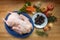 Raw duck ready to cook and ingredients such as apples, baked plums, vegetables and herbs on a wooden kitchen counter, high angle