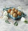 Raw eggs in a carton for eggs with white flowers on a marble white table, ready for painting Easter, selective focus