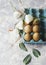 Raw eggs in a carton for eggs with white flowers on a marble white table, ready for painting Easter, selective focus