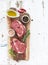 Raw fresh meat Ribeye steak entrecote and seasonings on cutting board over white wooden background.