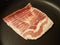 Raw frozen bacon strips in frying pan or skillet