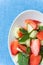 Raw fruit detox salad with cucumbers strawberries apples fresh mint in crystal bowl on blue table cloth background. Vegan
