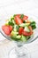 Raw fruit detox salad with cucumbers strawberries apples fresh mint in crystal bowl on white wood kitchen table