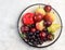 Raw fruits - apples, pears, plums and gooseberries on a round plate on a light gray background