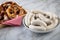 Raw German Bavarian WeiÃŸwurst white sausage chain on plate and chives and butter pretzels in basket on marble background