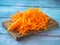 Raw grated carrots lying on a cutting board on a blue wooden table, rustic style