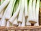 Raw green fresh organic whole Leeks with the white bulb close up at a market, background white and green leek stalks in a basket