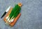 Raw green onions and crocheted green onions lie on wooden board. Cutting knife lies near wooden board. Grey background of felt