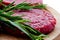 Raw hamburgers with cellophane and rosemary on wooden board