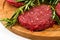 Raw hamburgers with cellophane and rosemary on wooden board