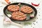 Raw hamburgers - cutlets from organic beef meat with garlic, chilli and rosemary in a frying pan on a white background