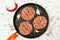 Raw hamburgers - minced meat from organic meat with cloves of garlic, hot chili pepper and rosemary in a frying pan on a white