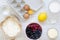 Raw ingredients: berries, flour, eggs, butter, lemon, water, sugar, salt for cooking berry pie on white wooden surface, top view.