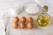 Raw ingredients for cooking classic omelette: six brown eggs, glass of milk, some flour and olive oil on a white wooden table.