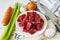 Raw ingredients for cooking stewed meat or goulash: pieces of fresh beef, carrot, onions, garlic, celery and salt on a white