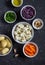 Raw ingredients - potatoes, cauliflower and red cabbage, green onions, carrots, nuts and olive oil in the bowls on a dark stone ba