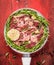 Raw lamb loin chops with rosemary and garlic in white frying pan on red wooden background, top view