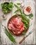 Raw leg of lamb with meat fork and fresh herbs for cooking on white wooden background