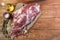 A raw leg of mutton on a bone lies on a piece of burlap , onions, garlic, pepper, salt,rosemary and vegetable oil on a wooden