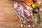 A raw leg of mutton on a bone lies on a piece of burlap , onions, garlic, pepper, salt,rosemary and vegetable oil on a wooden