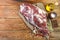A raw leg of mutton on a bone lies on a piece of burlap , onions, garlic, pepper, salt,rosemary and vegetable oil on a wooden