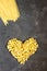 Raw macaroni - pasta Conchiglie. In the middle of the empty space in the shape of a heart on a dark concrete background.
