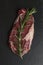 Raw marbled beef ribeye steak with rosemary sprig. A piece of meat with fatty veins on a stone black board. Top view. Vertical