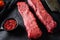 Raw marbled beef steak near butcher knife with pink pepper and rosemary. Black background. Side view