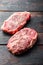 Raw marbled beef steak, top blade organic meat cut. On dark wooden background, side view