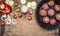 Raw meat balls in vintage cast-iron pan with tomatoes, onions and peppers, herbs on wooden rustic background top view close up