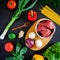 Raw meat in plate on wooden board and fresh vegetables on dark background. Top view. Flat lay. Food background
