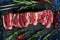 Raw meat ribs on a black stone plate, decorated with green sprigs of rosemary,