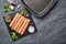 Raw meat sausages on a slate board, with herbs and spices and a square grill pan. View from above