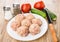 Raw meatballs in plate, salt, peeper, vegetables and knife