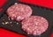 Raw minced beef burgers in plastick vacuum tray on red background