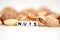 Raw mixed nuts and the word â€œnutsâ€ spelled by tiled letter beads spread on a white table