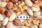 Raw mixed nuts and the word â€œnutsâ€ spelled by tiled letter beads spread on a white table