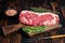 Raw new york strip beef steak or striploin on a wooden board. Dark wooden background. Top view