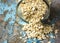 Raw oatmeal is scattered on the desk of the bank in which the oat flakes are stored. blue background in the style of Shabby Chic.