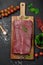 Raw organic marbled beef with spices on a wooden cutting board on a black slate, stone or concrete background