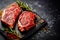 Raw organic marbled beef steaks with spices on a wooden cutting board on a black slate, stone or concrete background